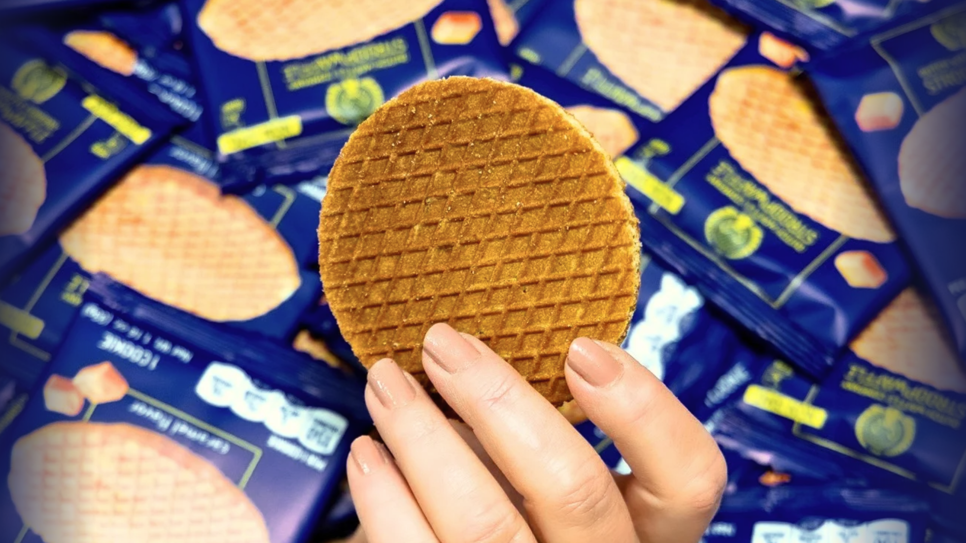 Hand holding a round cookie above blue packages with cookies