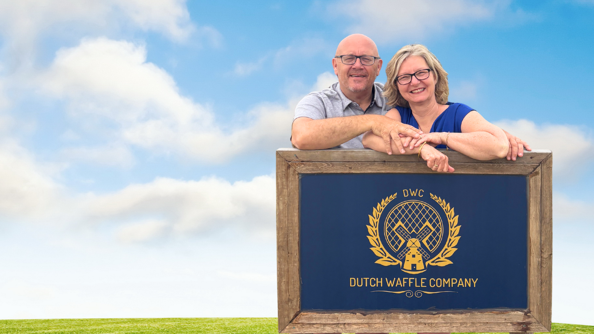 Two people posing behind a sign for the Dutch Waffle Company against a blue sky.